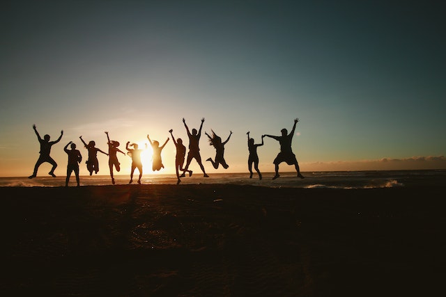 a group of people in a line jumping and posing for the camera at sunset